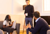 A man standing having a conversation with a male and female sitting down