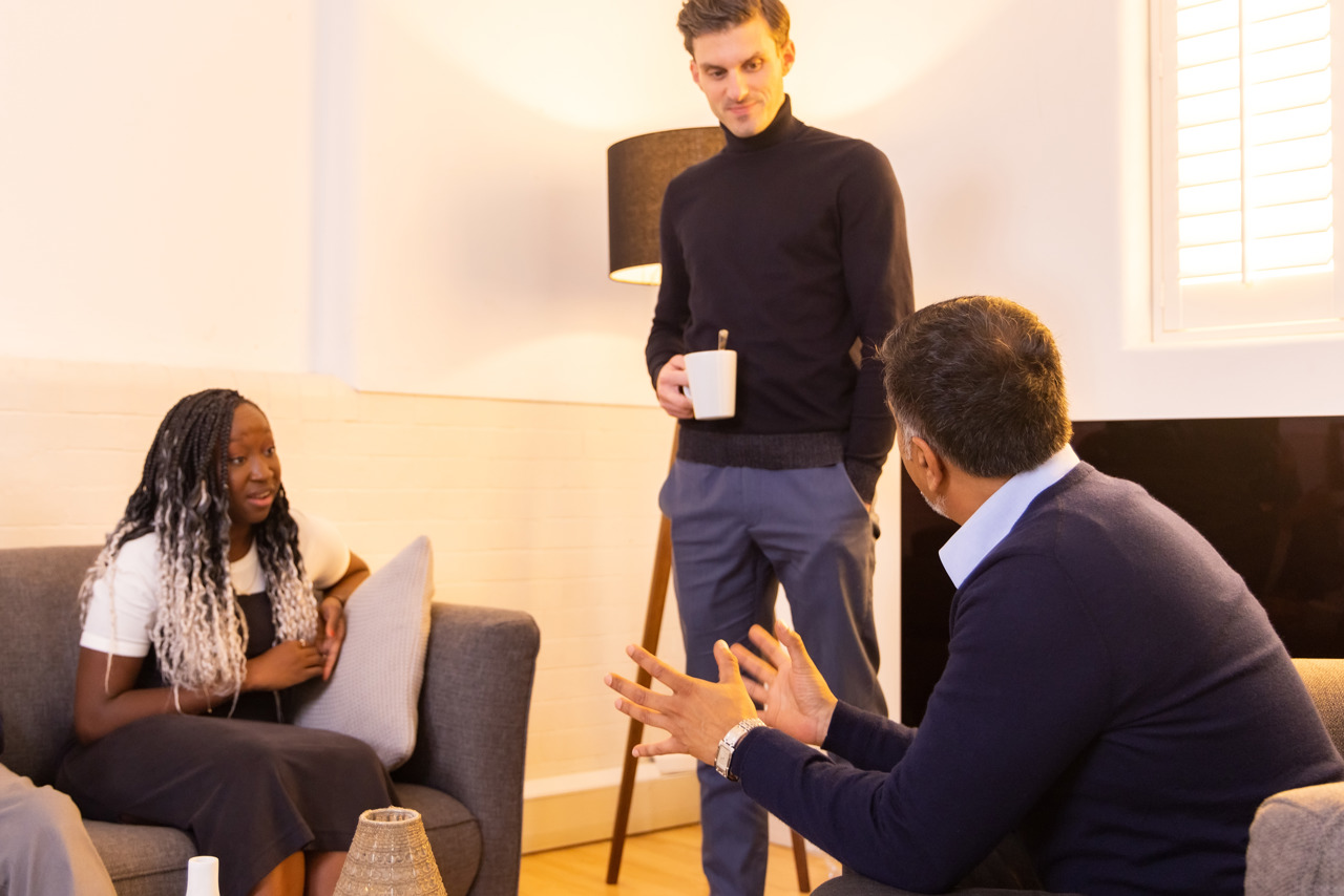 A man standing having a conversation with a male and female sitting down