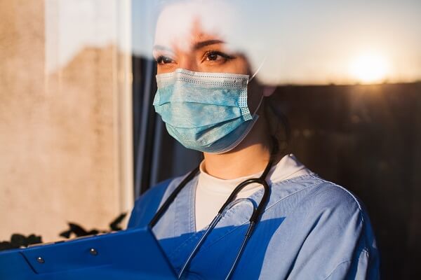 A medical professional wearing a face mask and looking out of a window